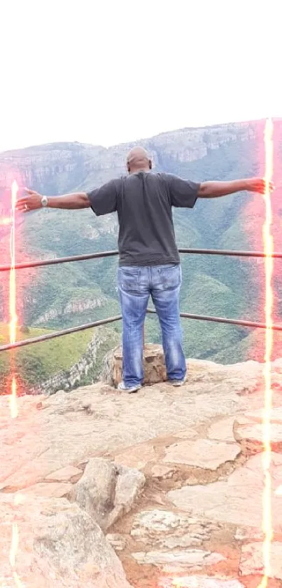 Man standing on rocky overlook with outstretched arms in mountain vista.