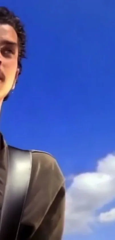 Musician stands with guitar under a bright blue sky.