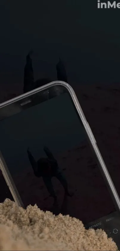 Phone partially buried in sand reflects a dark scene.