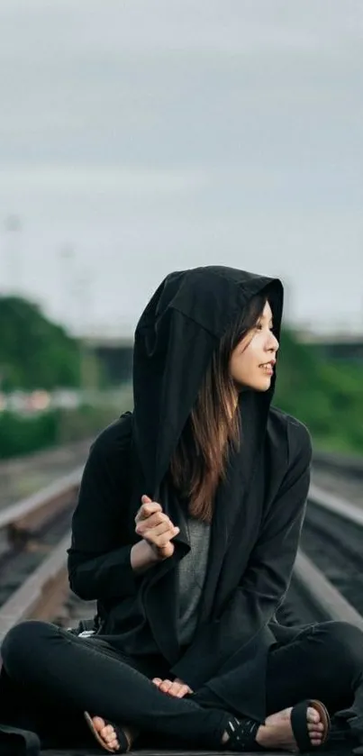 Hooded girl sitting on train tracks in urban setting.