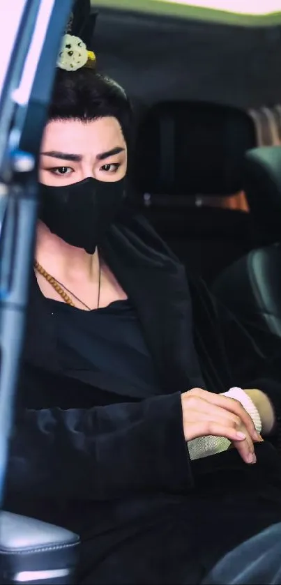 Person in black mask and attire seated in a car.