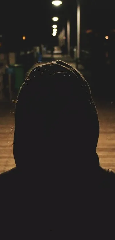 Silhouette of a hooded figure on a dimly lit night path.