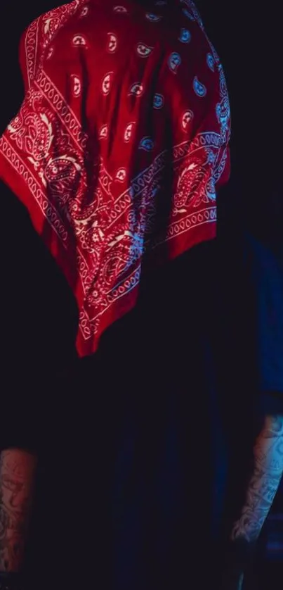 Silhouette with red bandana and tattoos in dark setting.