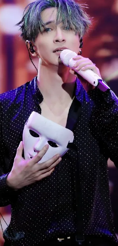 Performer holds mask on stage, under dramatic lighting.