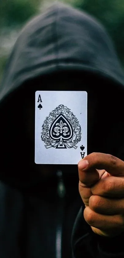 Hooded figure holding Ace of Spades card in mystery-themed wallpaper.