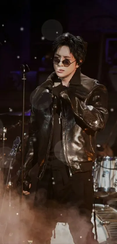 Stylish performer on stage in dark ambiance with leather jacket and sunglasses.