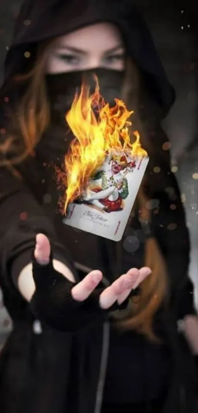 A hooded figure holds a flaming joker card.