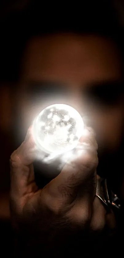 A hand holding a glowing mystical moon against a dark background.