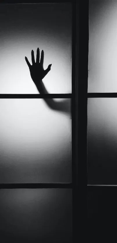 Mysterious silhouette of a hand behind a paneled glass in grayscale.