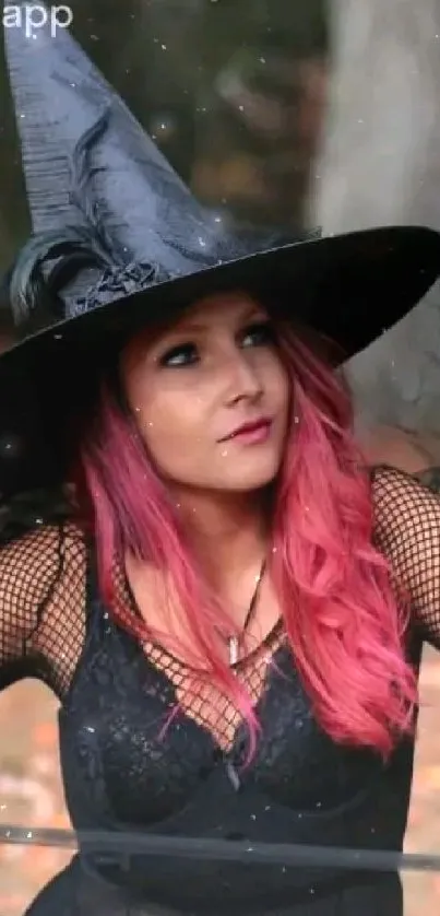 A witch with a black hat and pink hair against an autumn backdrop.