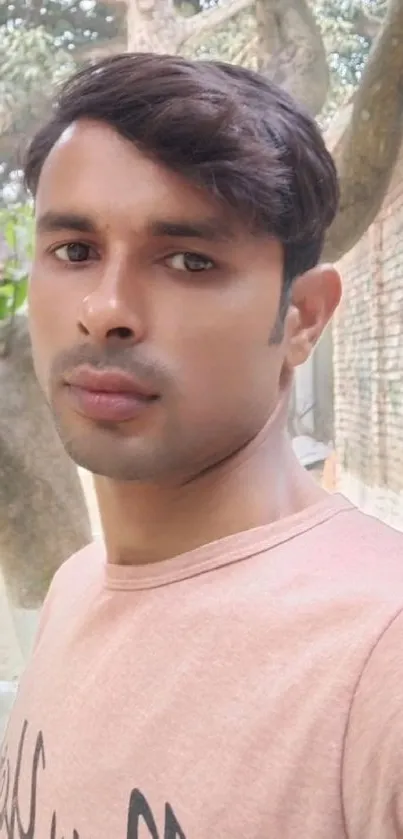 Man in pink shirt posing outdoors near a tree.