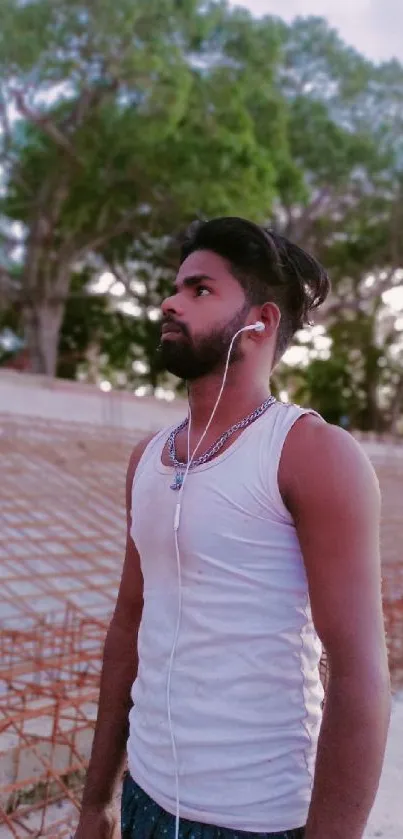 Man standing peacefully in nature, wearing white tank top and earphones.