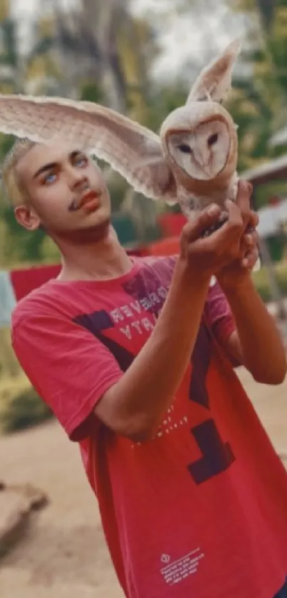 Young man in red shirt holding owl in a tranquil setting.