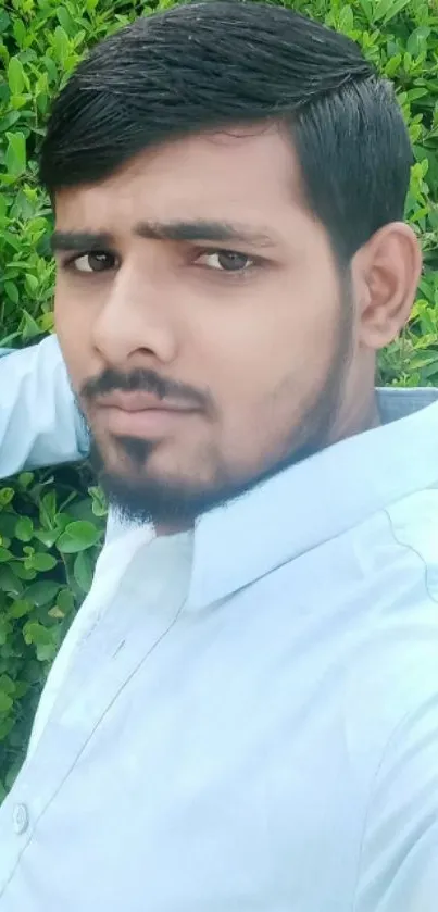 Man in white shirt posing against lush green leaves background.