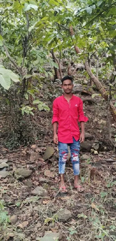 Man in red shirt standing in lush forest with vibrant greenery.