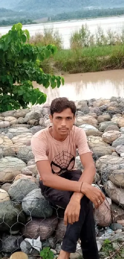 Person sitting on rocks by a serene river landscape.