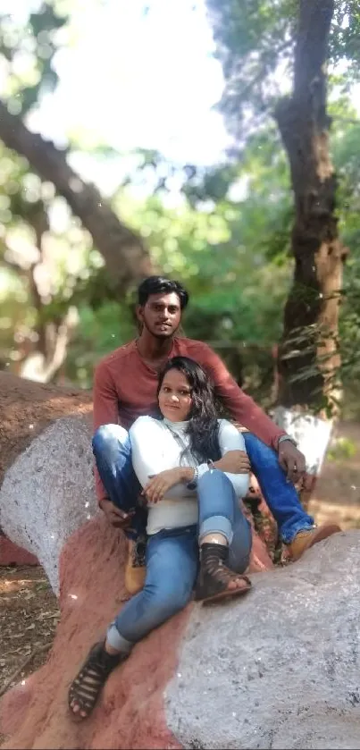 Couple sitting on a tree trunk in a lush, green forest.