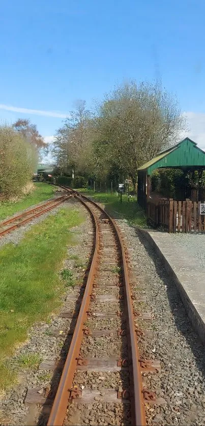 Scenic railway track with lush greenery and clear sky.