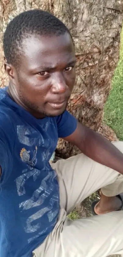 Man sitting under a tree, relaxed pose in nature.