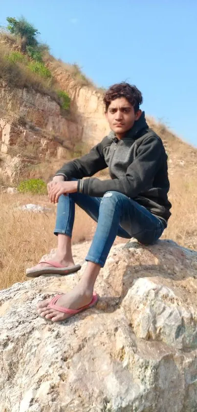 Person sitting on a rock in a natural outdoor setting with a scenic background.