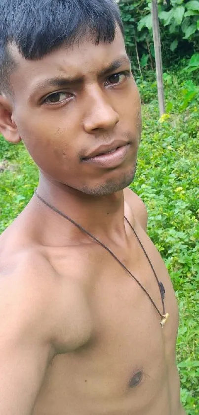 A young man takes a selfie in a lush green outdoor setting.