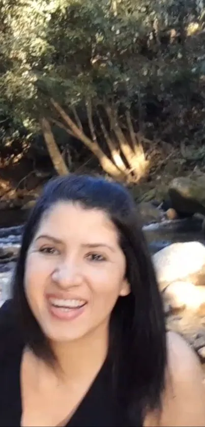 Woman smiling by a forest stream in nature scene.