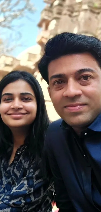 Couple taking selfie in front of ancient temple with lush nature.