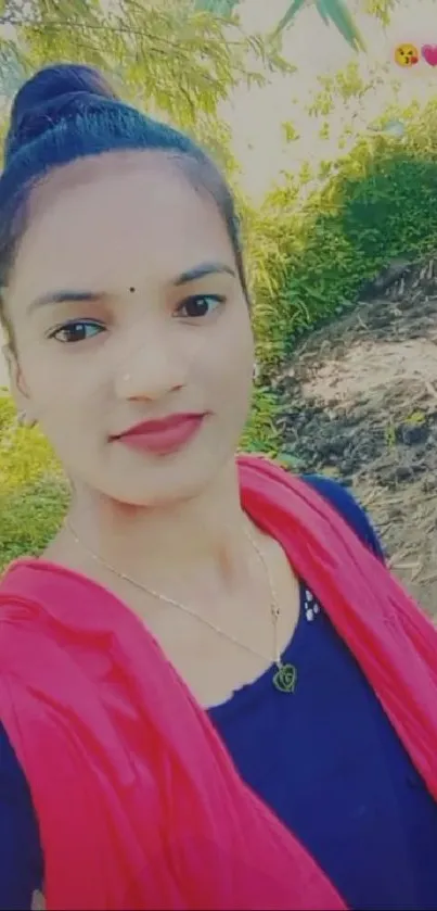 Young person smiling in natural outdoor setting with greenery.