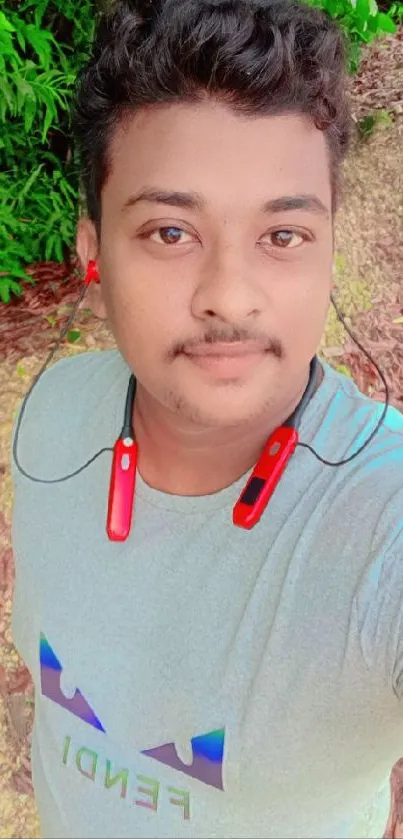 Man taking a selfie in a green, leafy setting outdoors.