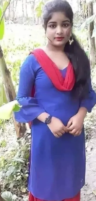 Person in blue dress with red shawl in lush green outdoors.