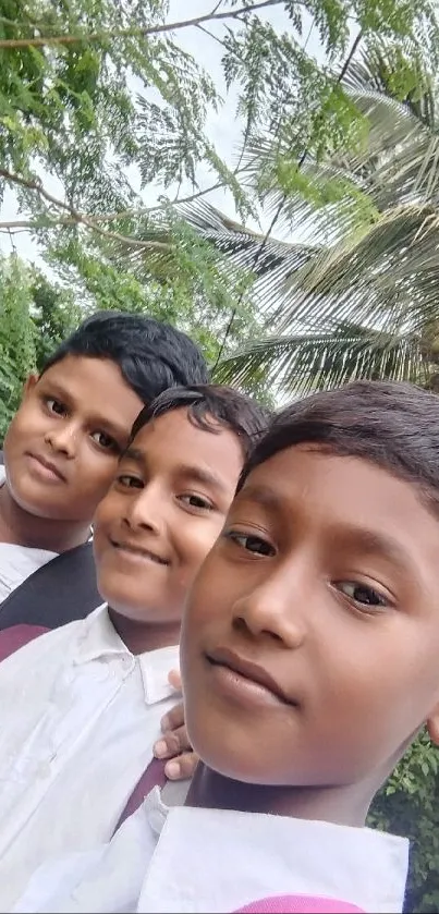 Three friends smiling under green trees.