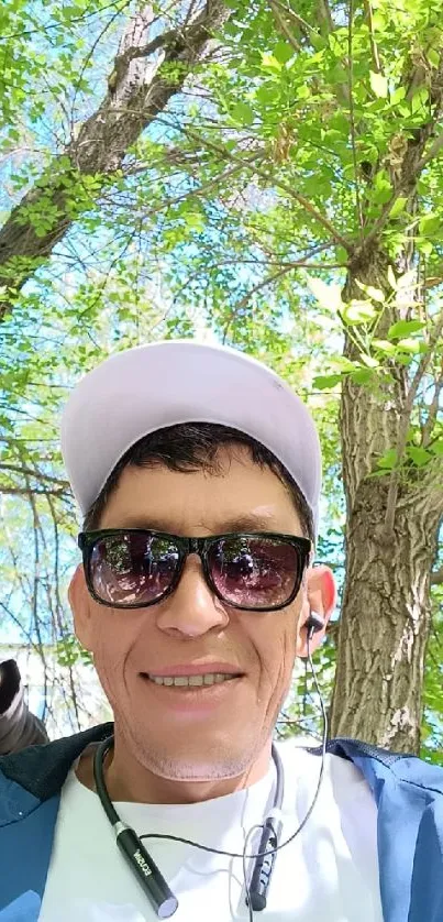 Man wearing sunglasses under leafy green canopy.