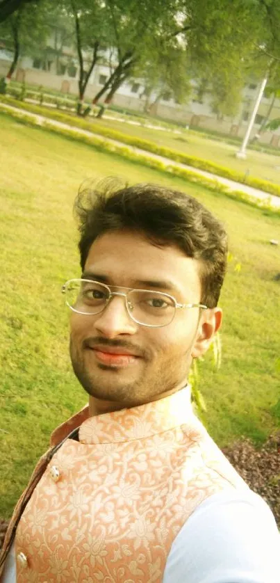 Man smiling in a lush green park with trees and grass around.