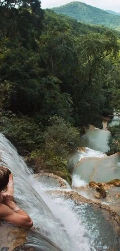 Man enjoying waterfall view amid lush green jungle.