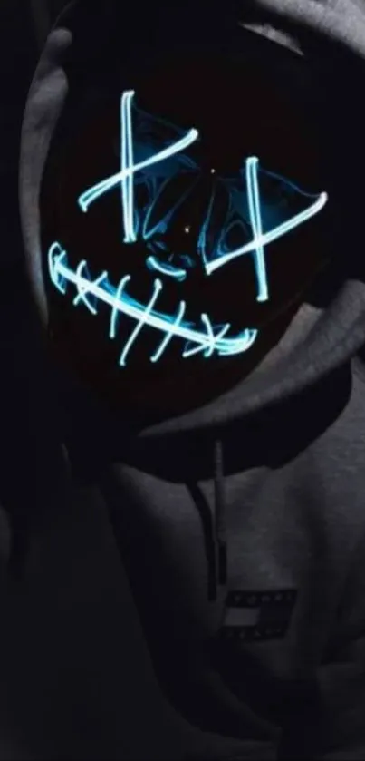 Dark figure wearing hoodie with neon mask glowing in blue