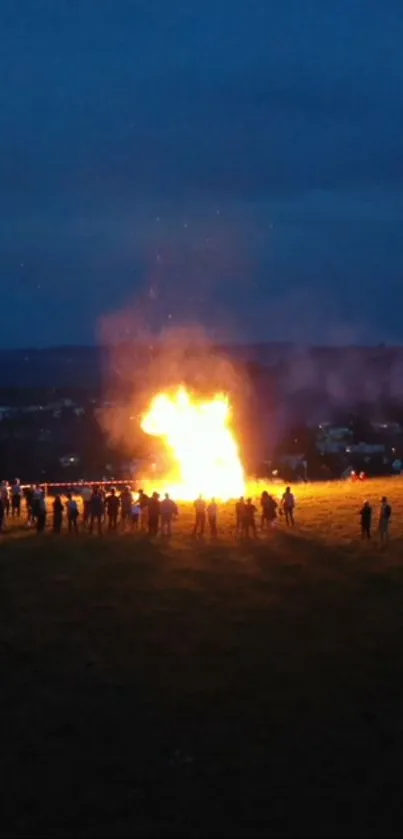 A bright bonfire in the night with people gathered around in a blue lit field.