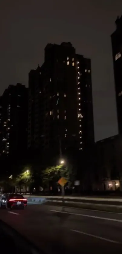 Dark city road with buildings illuminated by streetlights at night.