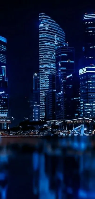 Night cityscape with blue-lit buildings reflecting in water.