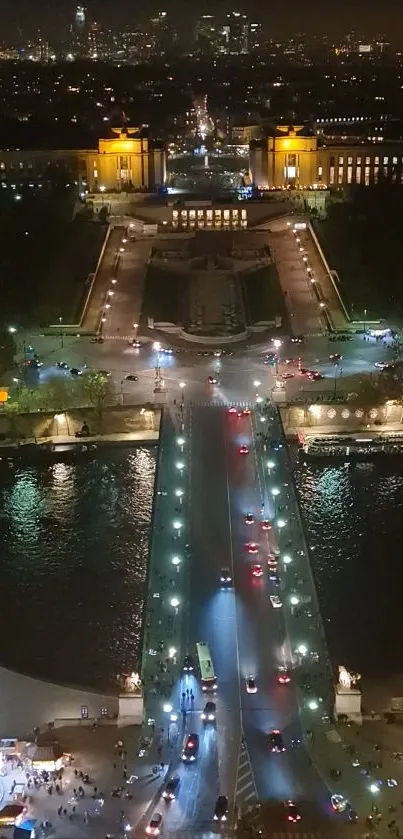 Aerial view of a brightly lit city at night with a bridge and shimmering water.