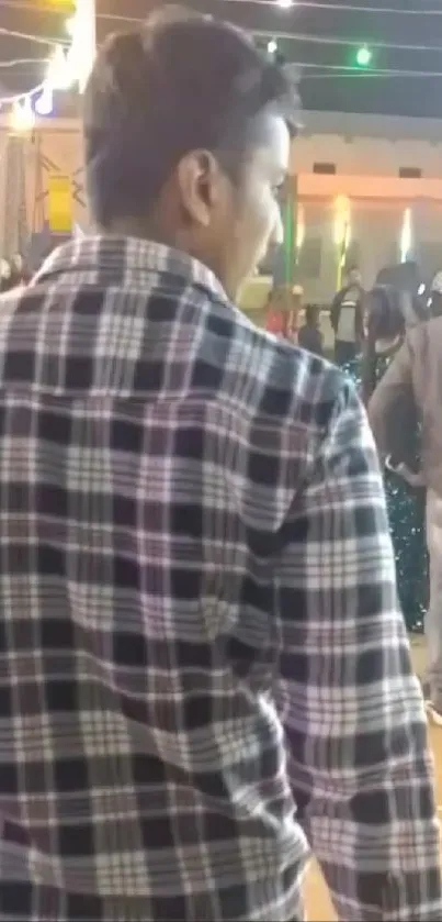 Man in checkered shirt at night festival gathering.