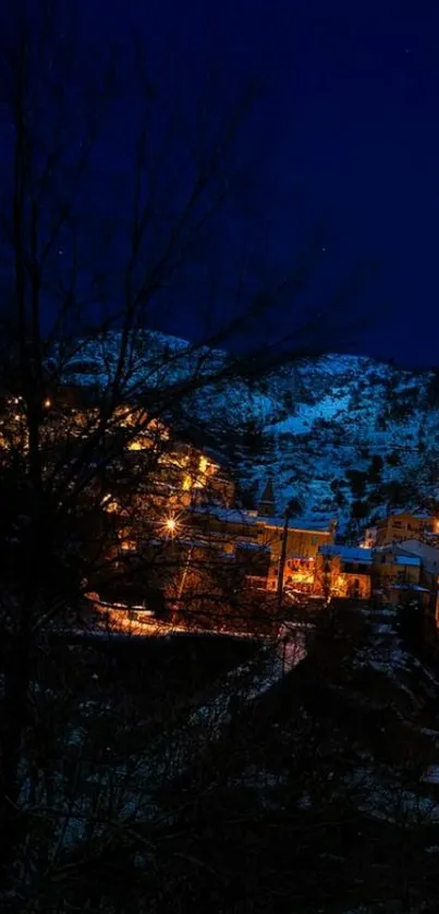 Night view of a mountain village with warm glowing lights and a dark blue sky.