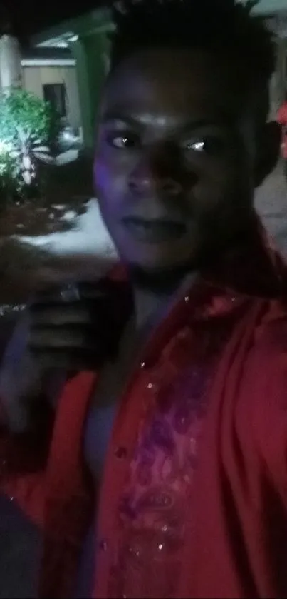 Person in a red shirt at night with an urban background.