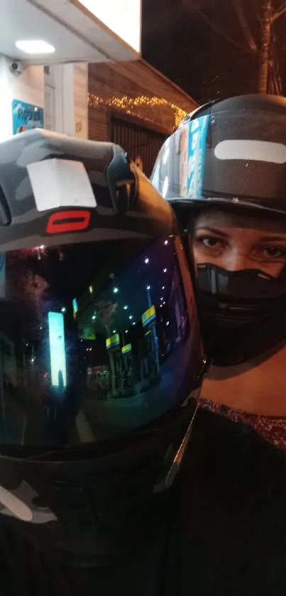 Two motorcyclists with helmets at night on a street.