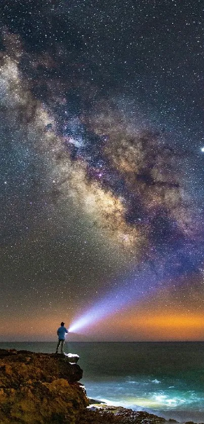 Person with flashlight under a starry sky by the ocean.