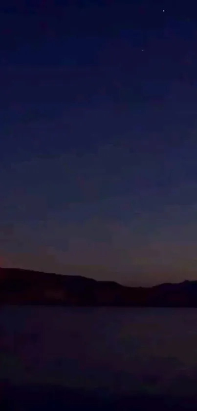 Night sky with horizon silhouettes and calm lake reflection.