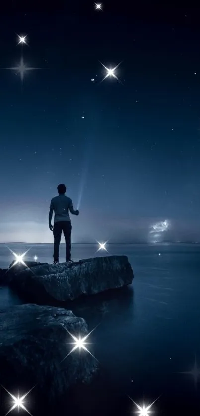 Man standing on rocks under a starry night sky by the ocean.