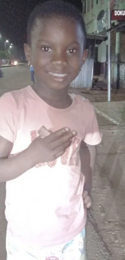 Child smiling on a dimly lit street at night.