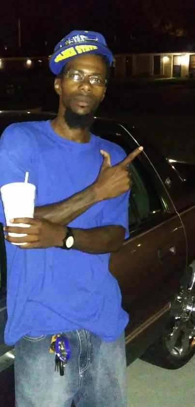 Man in blue shirt posing by car at night.