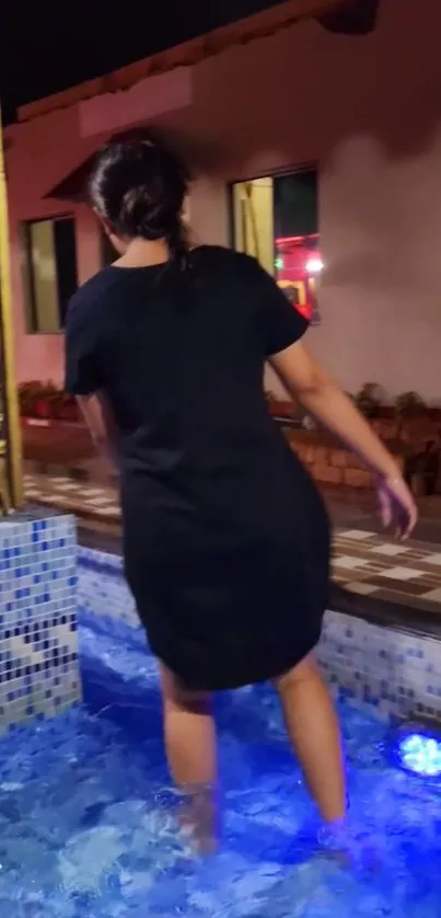 Woman in black dress walking in blue lit fountain at night.