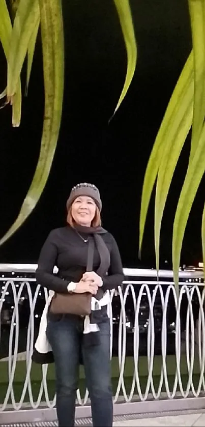 Person standing on a nighttime balcony with green leaves overhead.